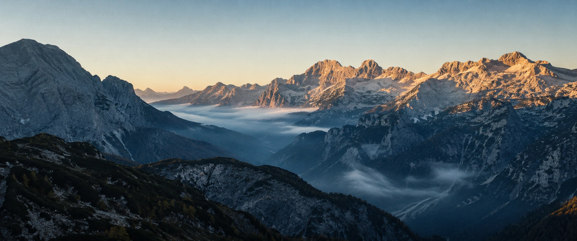 Dawn over an immense Alpine valley before any threat is visible.